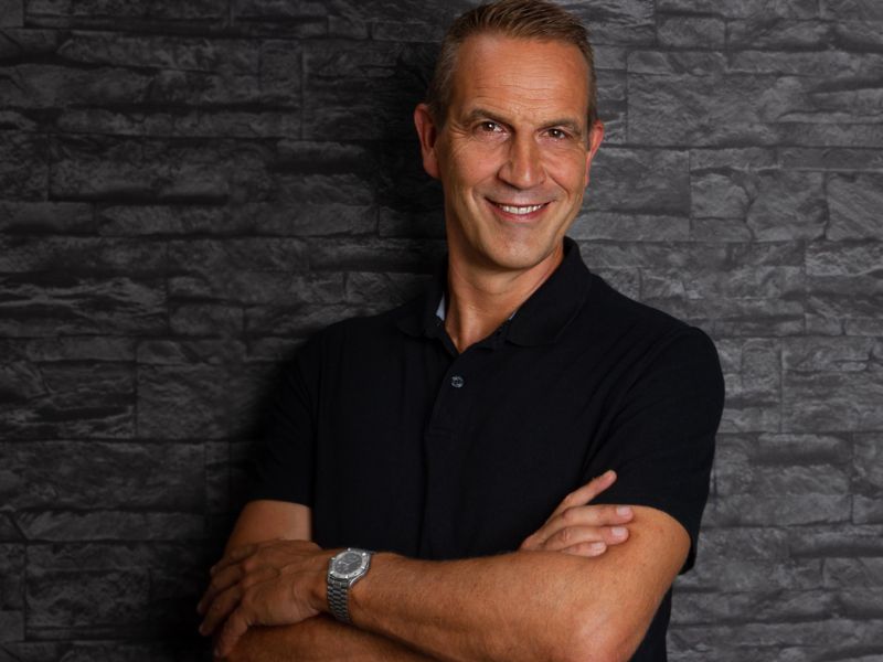 Mentalcoach Arnd Hebestreit mit verschränkten Armen vor einer schwarz gemauerten Wand. Er bietet Business Coaching in Mülheim an der Ruhr an.