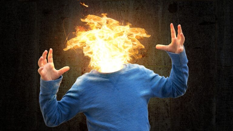 Eine Fotomontage eines Mannes im blauen Pullover, dessen Kopf als lodernder Feuerball dargestellt ist und der die Hände verzweifelt hebt. Das Bild visualisiert extreme körperliche Stressreaktionen und das Gefühl der totalen Überlastung bei Managern.